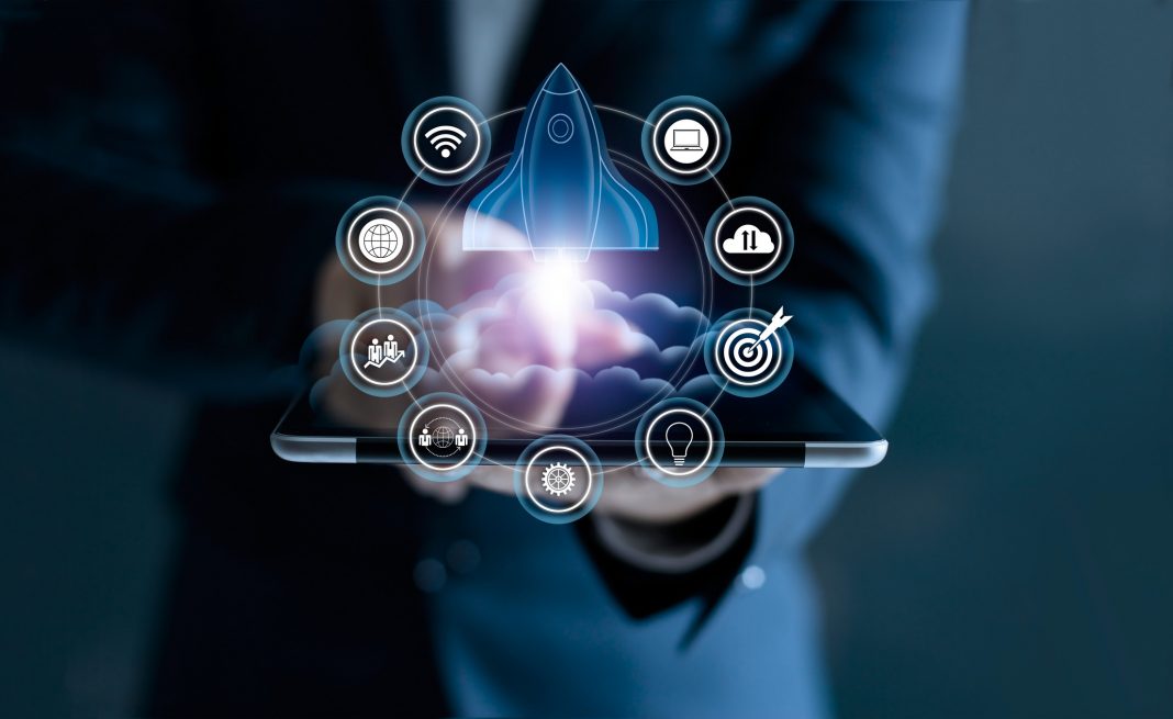 Startup concept. Businessman touching tablet and icon network connection with rocket flying out of screen on dark background